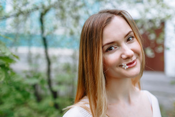 Naklejka premium Portrait of a girl in a white blouse holding a cherry blossom petal in her mouth