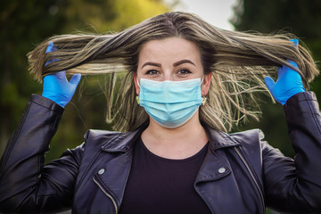 Young blonde hair woman with her face mask and blue rubber gloves is on the walking in the park. She is looking forward to the end of corona virus - COVID 19 and quarantine.