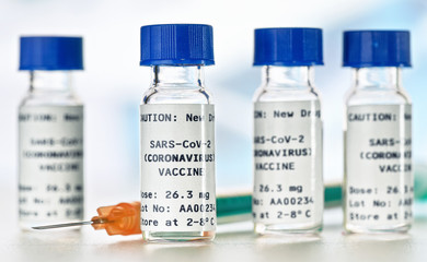 Coronavirus Covid-19 vaccine concept - small glass vials with blue caps on white table, closeup detail (own sticker design with dummy data - not real product)
