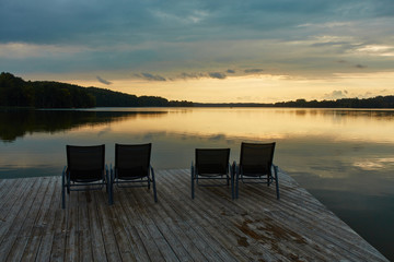 An empty pier with deckchairs on a calm lake, at sunset