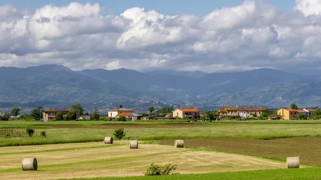 Beautiful landscape in the Tuscan countryside between the provinces of Pisa, and Lucca with hay bales in the foreground and Mount Abetone in the background, Italy, time lapse motion