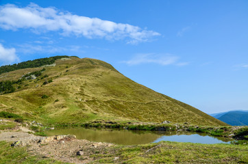 Beautiful mountain landscape, clouds on the blue sky with high green hills, rocks and lake. Carpathians, Ukraine