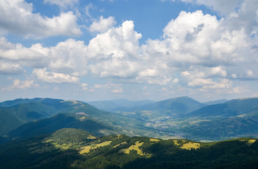 Naklejka na ściany i meble Beautiful landscape from a height. Typical Carpathian village in a valley, forest and mountains under blue sky with white clouds. Carpathians, Ukraine