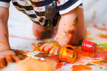 Cropped cheerful grimy baby crawls on the floor playing with paint. dirty kid close up. Happy...