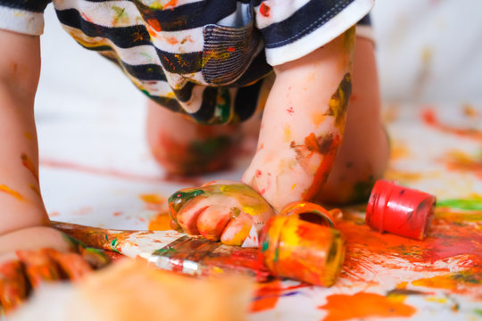 Cropped cheerful grimy baby crawls on the floor playing with paint. dirty kid close up. Happy leasure and play at home.