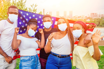 Group of girls and boys in medical mask smiling with American flag in spring park autumn evening...