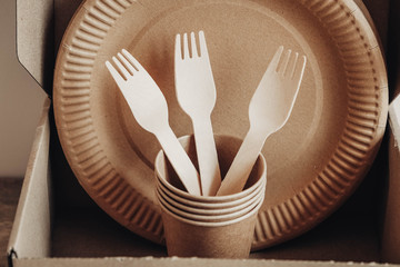 Wooden forks and paper cups with plates on kraft paper background. Eco friendly disposable tableware. Also used in fast food, restaurants, takeaways, picnics. Top view. Copy, empty space for text