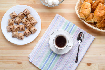 Cup of coffee on napkins on a wooden table with croissants and waffles.