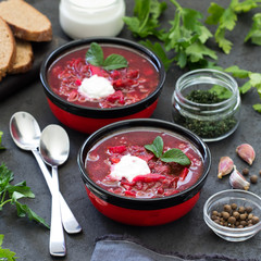 Beetroot soup with greens and sour cream in a bowl on a linen napkin on a dark background 