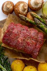 Raw roast beef on a board with a vegetable is sent to the oven. Raw meat of red beef with green rosemary and fresh vegetables on a wooden cutting board. Raw meat. Beef fillet with rosemary and spices.