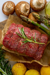 Raw roast beef on a board with a vegetable is sent to the oven. Raw meat of red beef with green rosemary and fresh vegetables on a wooden cutting board. Raw meat. Beef fillet with rosemary and spices.