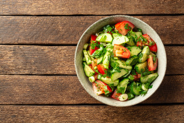 Fresh vegetable salad with cucumber, tomato and greens in bowl on rustic wooden table