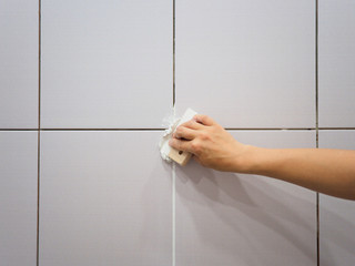 Grouting between tiles in the bathroom. Female hand holds a spatula. Repairs - obrazy, fototapety, plakaty