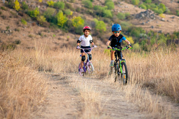 Fototapeta na wymiar Happy girl and boy having fun in autumn park with a bicycle on beautiful fall day. Active kids wearing bike helmet