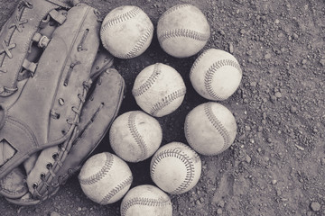 Old used practice baseballs with ball glove in monochrome, laying on field dirt with view from above.