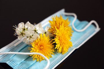 Spring flowers on medical mask isolated on black glass background. Concept of protection from pollen allergy