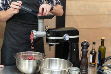 Chef putting raw meat into an electric grinder