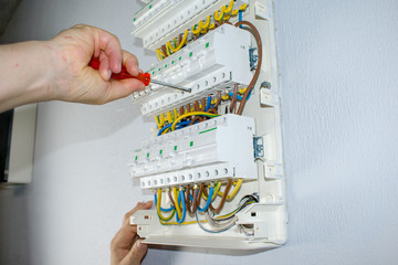 A male electrician works in a switchboard with an electrical connecting cable, fuses. Connects the...