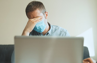 Tired man in medical mask working on the computer indoors.