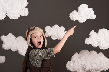 a girl dressed in a retro style jacket and helmet with glasses and dreams of becoming a pilot, clouds of cotton wool, gray background, tinted in brown