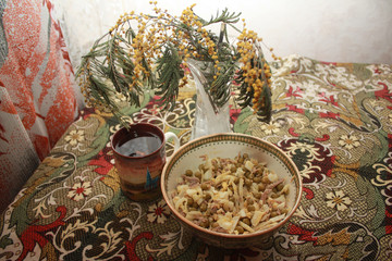 A bowl with olivier salad, a cup of tea and a bouquet of mimosa flowers on a table covered with a colored tablecloth.