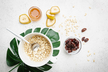 Bowl of oatmeal for porridge with ingredients banana, honey and raisins on white background, healthy breakfast every day, diet food