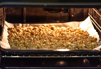 Pile of cashew nuts on a baking sheet in the oven. Roasting or drying cashew nuts in the oven, soft...