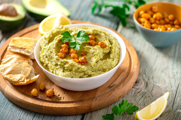 Cooked hummus with avocado in a white bowl on a server table closeup. Tasty and healthy vegetarian food, arab cuisine.