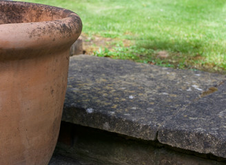 Naklejka premium Edge of terracotta pot beside step in green lawned garden