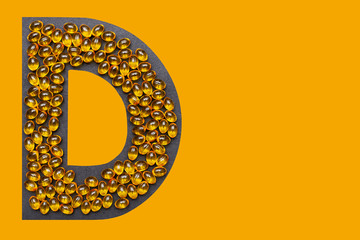 Vitamin D capsules laid out in the shape of the letter D on a orange background