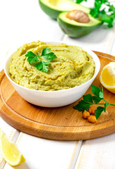 Cooked hummus with avocado in a white bowl on a server table closeup. Tasty and healthy vegetarian food, arab cuisine.
