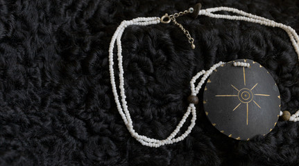 Plakat bijouterie. the necklace lies on a black sheep skin. contrast. the stones shimmer from the natural sun color.