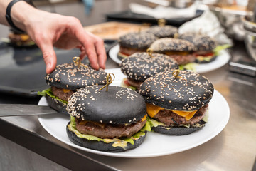 Man putting finished black burgers onto a plate