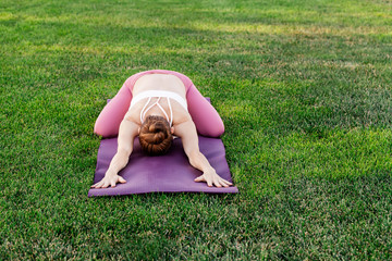 Young woman practicing yoga on a green grass, stretching and relaxing outdoor