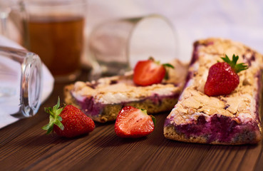 Wooden dark background of planks, white cloth, glasses with tea and homemade pie with cherries and strawberries. Delicious pastries for breakfast.