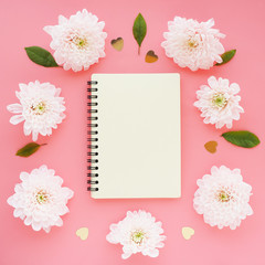 .a light yellow notebook on a spring and light pink chrysanthemum flowers in a circle on a pink background. space for text..