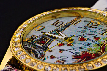 The picture shows a studio shot of a wristwatch with a gold rim set with beautiful stones.
The clock face shows an image of the Eiffel Tower