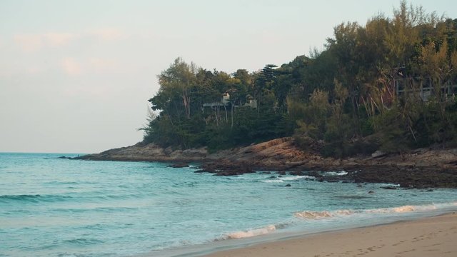 Beautiful sea cliffs wide shot on Nai Thon beach in Phuket, Thailand. Rolling waves breaking on the rocks early in the morning.