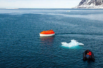 Maneuvering orange lifeboat in water in Arctic waters, Svalbard. Abandon ship drill. Lifeboat...