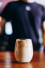 transparent glass with foamy coffee with milk and ice, summer version of Dalgano coffee on the bar table in a cafe