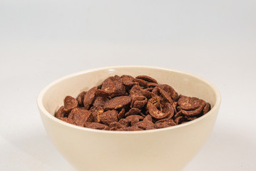 Chocolate corn flakes falling to the white bowl isolated on white. Motion.
