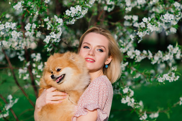 Attractive young woman holding dog spitz outside and smiling at camera, walking in the park.