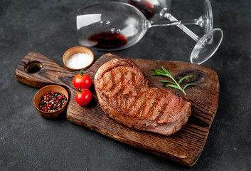 grilled beef steak with spices on a cutting board and glasses of red wine
 on stone background