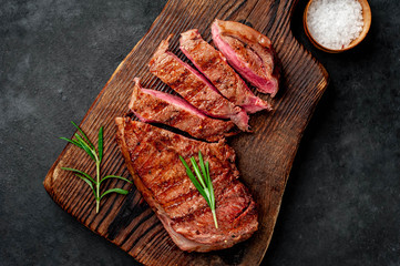 grilled beef steak with spices on a cutting board on a stone background