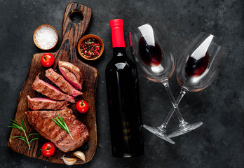 grilled beef steak with spices on a cutting board and a bottle of red wine, glasses on a stone background