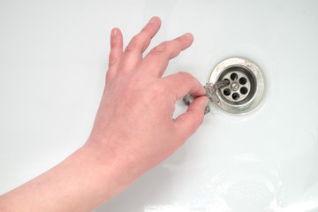 A man's hand pulls garbage out of the bathtub drain. The solution to the problem of clogged drain