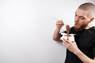 Fototapeta premium young man in a black T-shirt eats noodles from boxing on a white background