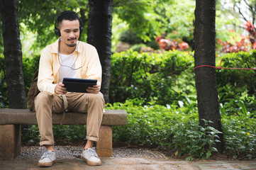 A young man wearing headphones and using a tablet in the park Relaxing atmosphere after a horrible disease outbreak