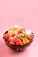 Summer tropical salad of watermelon, melon and mango in coconut bowl on pink. Vertical. Space for text. Clean eating.