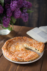 tasty piece of spinach pie and Chees Feta sprinkled with sesame seeds and with lilac flower in the background